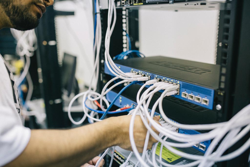 An IT support person plugs ethernet cables into a hub