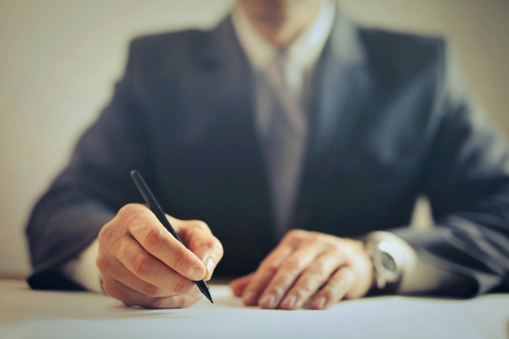 A torso of a male professional in a suit. They are signing a contract